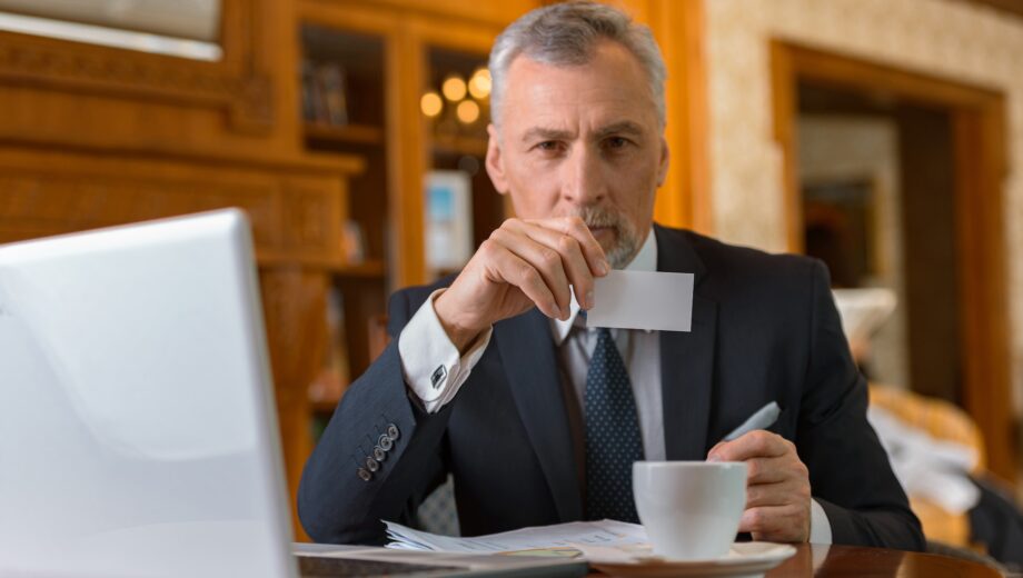 Adult businessman sitting on business meeting and holding visit card