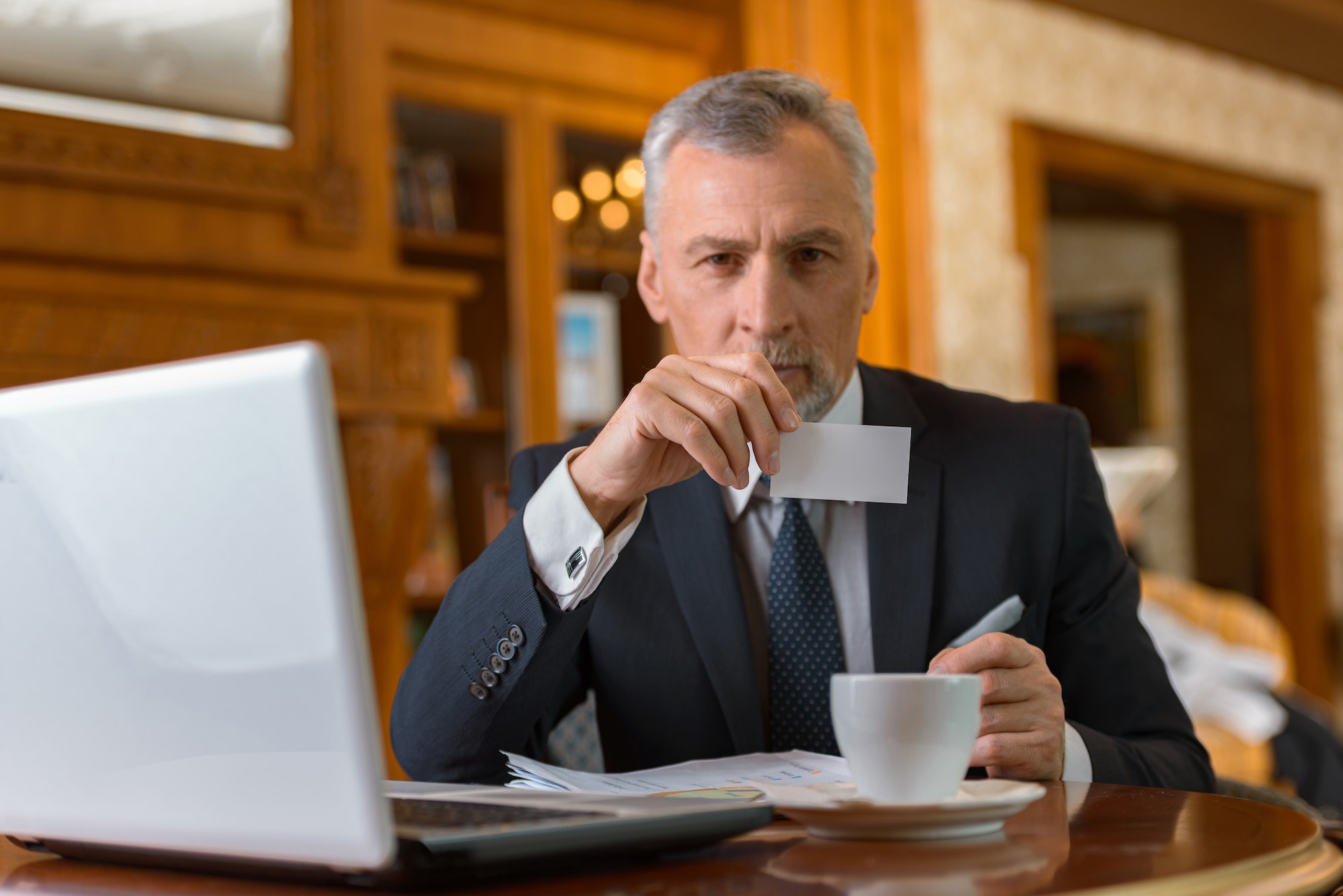 Adult businessman sitting on business meeting and holding visit card